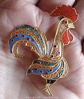 Front view showing red, blue, green enamel and detailed brass filigree in rooster shape