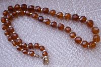 Full view of the faceted cognac amber bead necklace laid out on a fabric surface showing the size gradation and gold-toned spacer beads and clasp.
