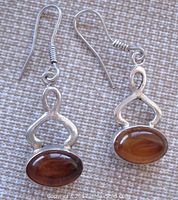 Pair of amber and silver dangle pierced earrings displayed against fabric background, front view showing amber cabochons and silver frames.
