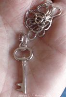 Close-up photo showing sterling silver key pendant held in hand with attached bail and part of chain visible