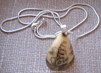 Photo showing front side of teardrop bone pendant with detailed sailing ship scrimshaw engraving, attached to silver chain.
