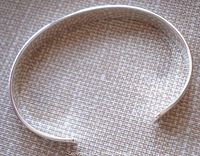Top view of the open-ended sterling silver bangle against a textured surface showing shape and finish.