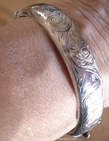 Close-up photo of the engraved floral and swirl patterns on the silver bangle bracelet worn on a wrist.