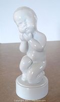 Front view of the white glazed porcelain infant figurine showing facial details and posture.