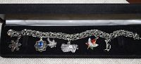 Sterling silver charm bracelet with six assorted charms displayed in a box, including enameled maple leaf charm.
