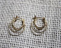 Front view of pair of 14K gold small triple hoop earrings with twisted design, lying flat on textured white fabric.
