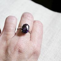 Side angle of the ring worn on a finger showing the size and deep purple faceted amethyst stone.