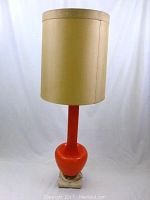 Front view of the lamp fully assembled with beige fabric shade on top, showing orange glass base and marble bottom.
