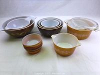 Group of 14 vintage glass and ceramic bowls arranged on white surface, showing variety of sizes and styles including brown and tan Pyrex and amber Federal glassware.