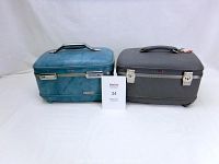 Two hard bodied vanity cases, one blue and one grey, shown closed on a white background with an auction lot card between them.