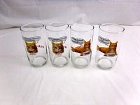 Four clear glass tumblers featuring printed images of Morris the Cat from 9-Lives cat food, arranged side by side showing two of each design.