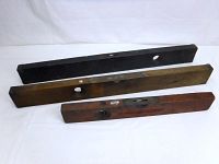 Three wooden vintage spirit levels laid out side by side, showing different wood finishes and sizes.