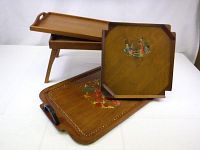 Four wooden trays displayed on white surface showing different sizes and decorative features including painted figures and floral designs.