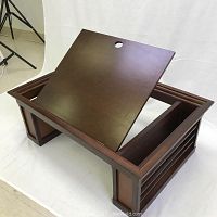 Wooden adjustable bed desk with a dark brown finish, showing the tilting surface angled up with cable hole visible.
