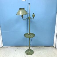 Full view of vintage green metal floor lamp with attached round table and metal base against blue background