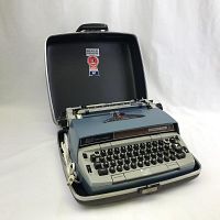 Front angle view of the Smith Corona Model 210 Automatic electric typewriter inside its hard carrying case, showing keyboard and ribbon area.