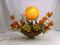 Front view of illuminated gold spaghetti ball lamp globe with floral-filled gold spaghetti boat base on marble block.