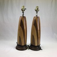 Front view of two wooden Mid Century Modern lamps with mixed wood patterns, brass lamp sockets, and round wooden bases.
