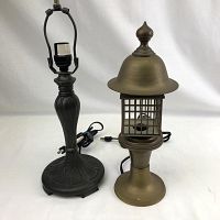 Photo showing two metal desk lamps side by side on a white background. The darker metal lamp has a decorative vertical ribbed body and base, 17 inches tall. The brass lamp has a mesh cage surrounding the bulb socket with a flared dome top, 15 inches tall.