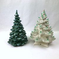 Two ceramic Christmas trees side by side on a plain background; white tree with green bulbs and base; green tree with white bulbs and no base