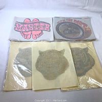 Lot includes two packages of gold glitter tiger face iron-on decal transfers, each package holding 25 sheets approximately 12 x 11 inches, with visible aged yellowing on the paper but mint condition decals inside.