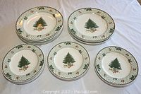Top view showing all 18 plates (9 dinner and 9 salad/dessert) stacked on a white cloth, showing the Christmas tree design and patterned rims.
