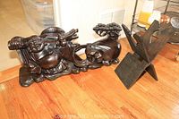 Wide shot showing the carved wooden Buddha statue reclining beside an adjustable magazine rack on wooden floor.