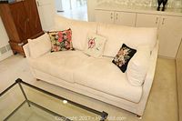 Front view of beige upholstered love seat with three floral embroidered decorative pillows.