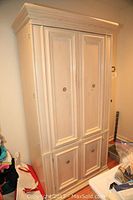 Front view of wooden armoire showing two upper doors and two lower doors with round metallic knobs.
