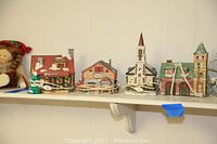 Full view of six snow village buildings on a shelf from left to right including a department store, a church, a general store, and other houses.
