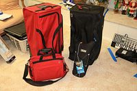 Two Victorinox travel bags: a black upright wheeled suitcase and a red shoulder bag, along with the CamelBak hydration pack on carpeted floor.