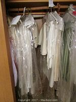 Photo of multiple white and light-colored table linens hanging on hangers, protected by plastic covering, stored in a closet or wardrobe.