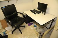 Desk and chair setup in basement office space showing drafting desk with computer monitor, keyboard, and mouse on top, and black office chair next to it.