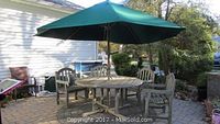 Full view of round teak table with four matching chairs and green umbrella on patio
