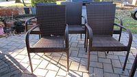 Five brown wicker outdoor arm chairs arranged on a stone patio showing front view.