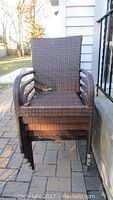 Five brown wicker stackable outdoor arm chairs stacked together on a stone patio beside a house.