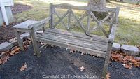Teak bench and side table outdoors on gravel with leaves around.