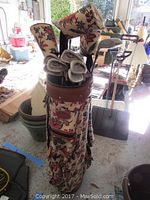 Full view of golf bag with clubs inside, floral patterned Bloomingbags golf bag with brown leather trim, multiple golf clubs including some with matching floral headcovers.