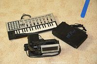 Lot items including Korg microKontrol keyboard, Sony PS2 console, and Canon VC 20A camcorder placed on carpet floor.