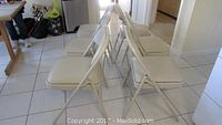 Side angle view of 6 beige vinyl cushioned folding chairs arranged in two rows, showing cushioned seats and metal frames.