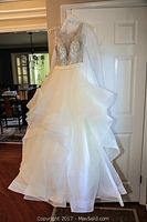 Front view of ivory Allure Couture gown on hanger against door, showing full layered skirt and beaded bodice