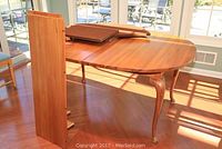 Oval maple dining table with two attached leaves visible, table pads on top, and four curved legs with carved upper parts.
