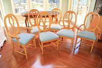 Set of 6 wooden dining chairs including 2 captain chairs with armrests and 4 side chairs. Light blue upholstery on seats. Shown on wood floor in well-lit room.