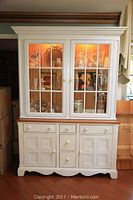 Front view of painted wood china cabinet showing upper glass hutch with interior lighting and lower buffet with drawers and doors