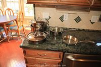 Five stainless steel cookware items set on kitchen counter including three Culinary Institute of America pots with lids and one Calphalon frying pan and lid