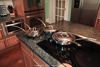 Three stainless steel pots and pans with lids arranged on a kitchen counter.