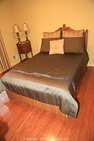 Full view of full size bed with carved wooden headboard, brown bedding, and pillows on hardwood floor
