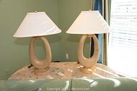Two matching lamps with oval open bases and white shades placed on a marble-top table