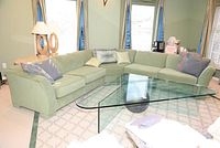 Full room view showing L-shaped green sectional sofa with glass coffee table