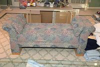 Front view of the tapestry settee showing floral patterned upholstery and wooden legs on a light green patterned carpet.